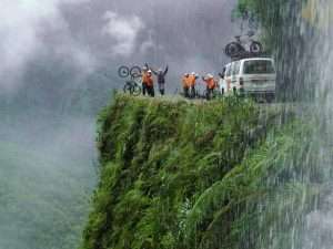 Cyclists on Bolivia Death Road riding along a narrow cliff with fog, jungle vegetation and extreme mountain scenery